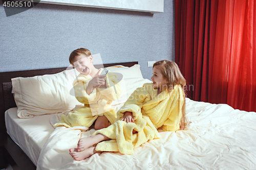 Image of Happy laughing kids, boy and girl in soft bathrobe after bath play on white bed