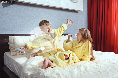 Image of Happy laughing kids, boy and girl in soft bathrobe after bath play on white bed