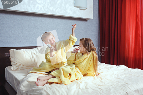 Image of Happy laughing kids, boy and girl in soft bathrobe after bath play on white bed