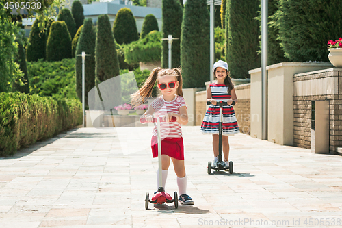 Image of Preschooler girls riding scooter outdoors.