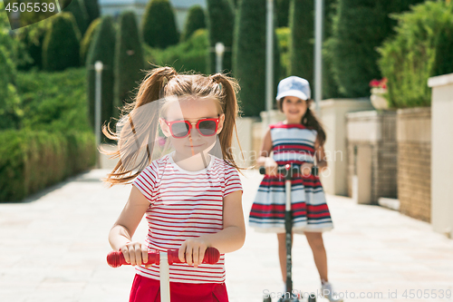 Image of Preschooler girls riding scooter outdoors.