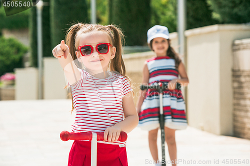 Image of Preschooler girls riding scooter outdoors.