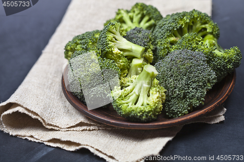 Image of Fresh green organic broccoli in brown plate and linen napkin.