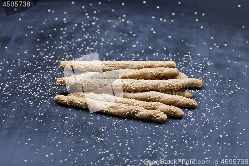 Image of Italian grissini or salted bread sticks with sesame seeds on bla