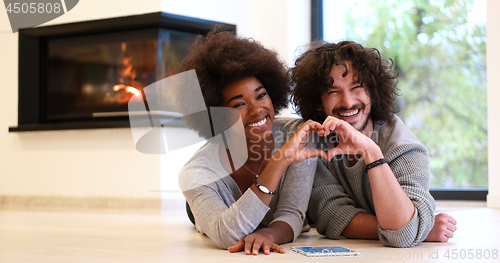 Image of multiethnic couple showing a heart with their hands on the floor