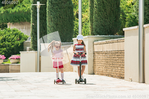 Image of Preschooler girls riding scooter outdoors.