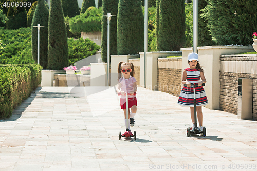 Image of Preschooler girls riding scooter outdoors.