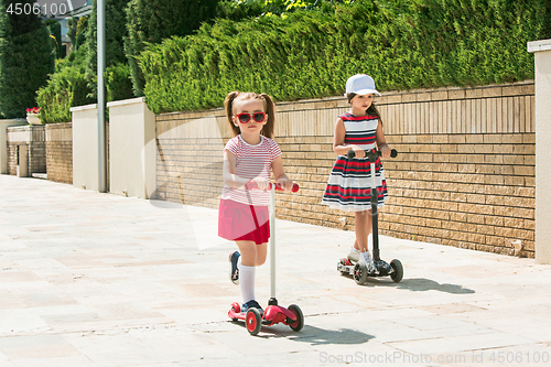 Image of Preschooler girls riding scooter outdoors.