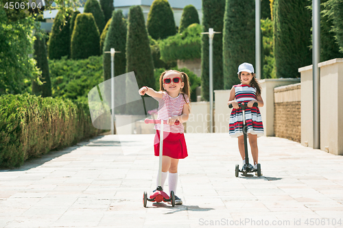 Image of Preschooler girls riding scooter outdoors.