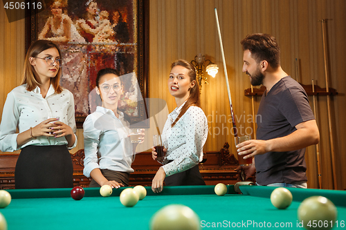 Image of Young men and women playing billiards at office after work.