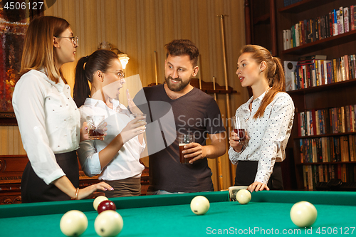 Image of Young men and women playing billiards at office after work.