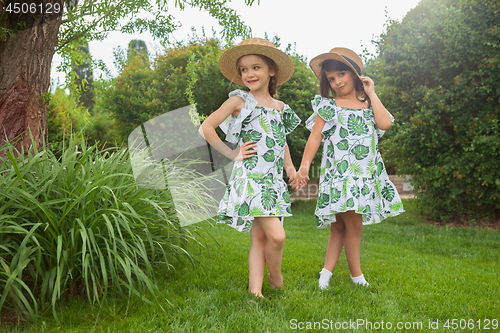 Image of Portrait of smiling beautiful girls with hats against green grass at summer park.