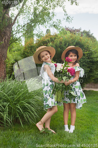 Image of Portrait of smiling beautiful girls with bouquet of peonies against green grass at summer park.