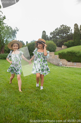 Image of Portrait of smiling beautiful girls with hats against green grass at summer park.
