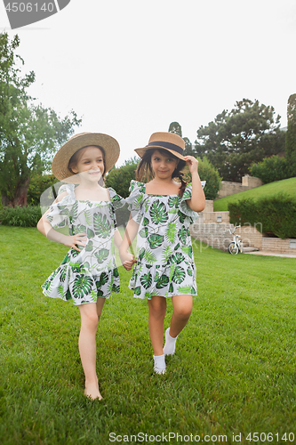 Image of Portrait of smiling beautiful girls with hats against green grass at summer park.
