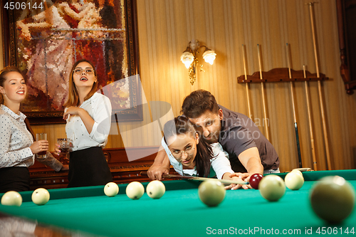 Image of Young men and women playing billiards at office after work.