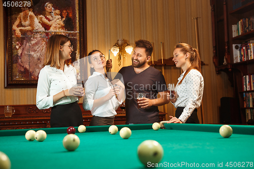 Image of Young men and women playing billiards at office after work.