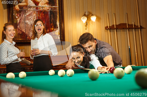 Image of Young men and women playing billiards at office after work.