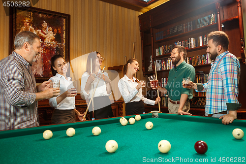 Image of Young men and women playing billiards at office after work.