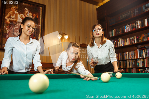 Image of Young women playing billiards at office after work.