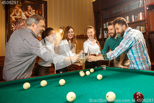 Image of Young men and women playing billiards at office after work.