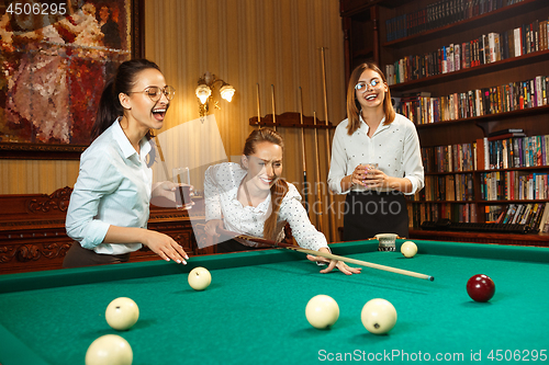 Image of Young women playing billiards at office after work.