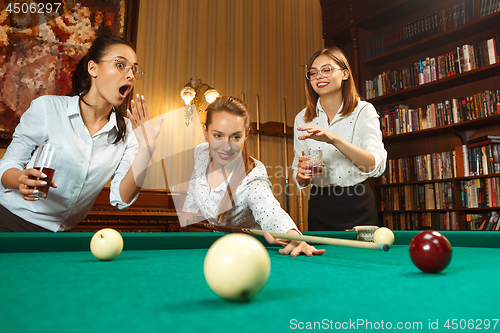 Image of Young women playing billiards at office after work.