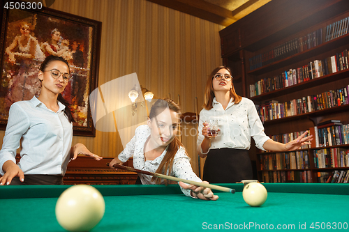 Image of Young women playing billiards at office after work.