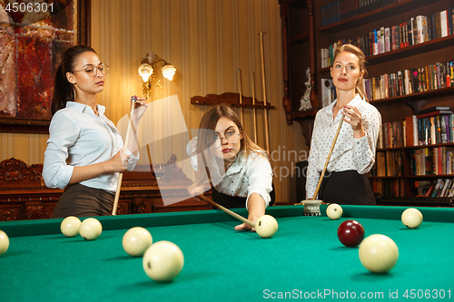 Image of Young women playing billiards at office after work.