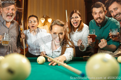 Image of Young men and women playing billiards at office after work.