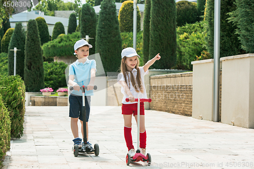 Image of Preschooler girl and boy riding scooter outdoors.