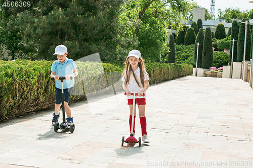 Image of Preschooler girl and boy riding scooter outdoors.