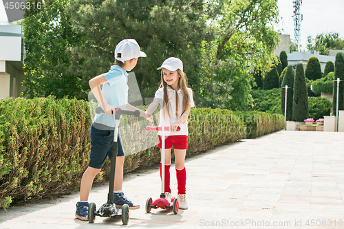 Image of Preschooler girl and boy riding scooter outdoors.