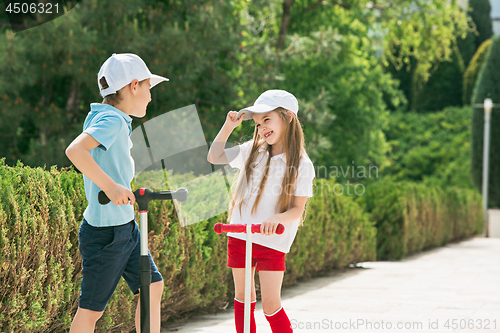 Image of Preschooler girl and boy riding scooter outdoors.