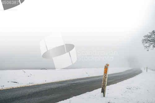 Image of Marker post by a misty road in the winter