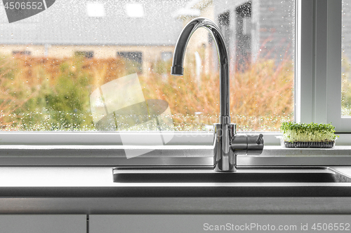 Image of Chrome faucet by a kitchen sink with a wet window