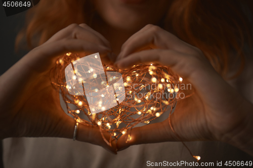 Image of Woman hands holding string of lights in the dark.