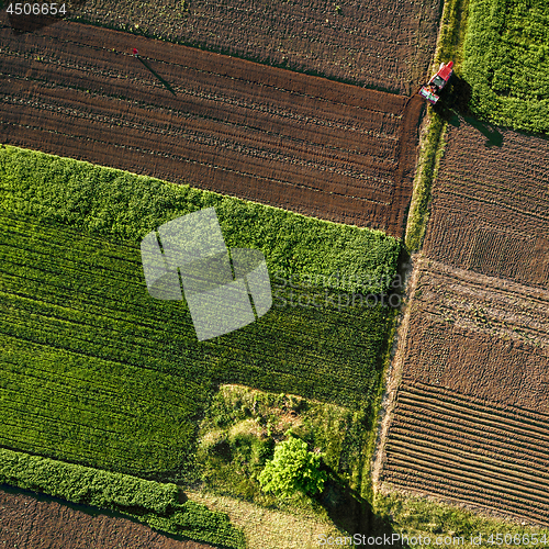 Image of Aerial view from the drone, a bird\'s eye view of agricultural fields with a road through and a tractor on it in the spring evening at sunset