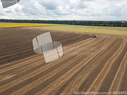 Image of An endless agricultural field after harvesting with tractor on it against a blue cloudy sky on a summer day.