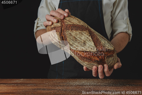 Image of Baker\'s hands hold an oval bread.