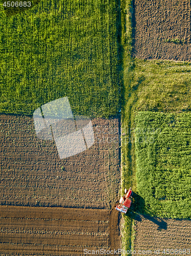 Image of Aerial view from the drone, a bird\'s eye view of agricultural fields with a road through and a tractor on it in the spring evening at sunset