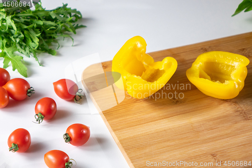 Image of Vegetables for salad.Cherry tomatoes, yellow pepper, arugula, on a white kitchen table.