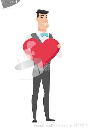 Image of Caucasian groom holding a big red heart.