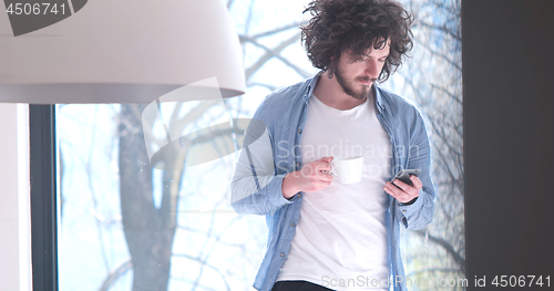 Image of young man drinking coffee and using a mobile phone  at home