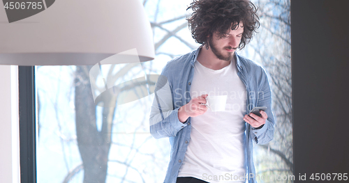 Image of young man drinking coffee and using a mobile phone  at home