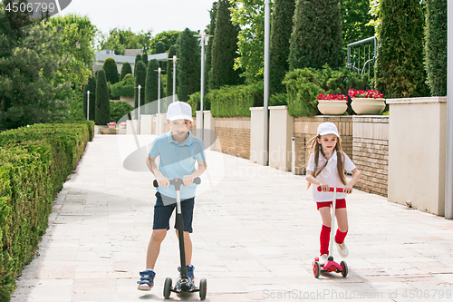 Image of Preschooler girl and boy riding scooter outdoors.