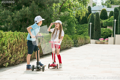 Image of Preschooler girl and boy riding scooter outdoors.