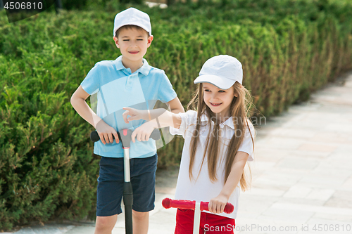 Image of Preschooler girl and boy riding scooter outdoors.