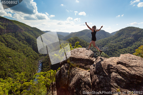 Image of Girl leaping on high rocky cliff with mountain river backdrop