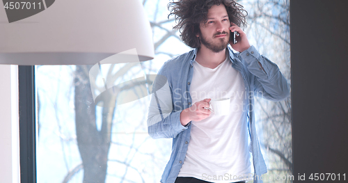 Image of young man drinking coffee and using a mobile phone  at home